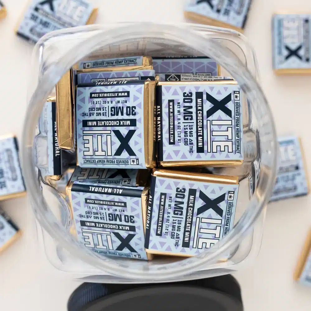 Top view of Xite Delta 9 Milk Chocolate Minis in a clear jar with purple labels and gold foil wrappers.